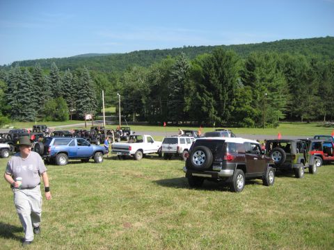 1991 Ford Bronco - A collection of SUVs and trucks are gathered in a grassy outdoor area on a sunny day.