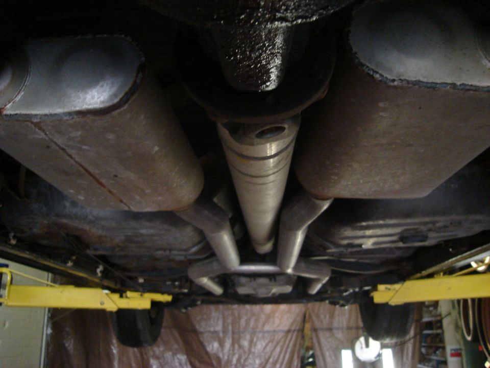 Underside view of a car's exhaust system and driveshaft, with a yellow lift pad visible