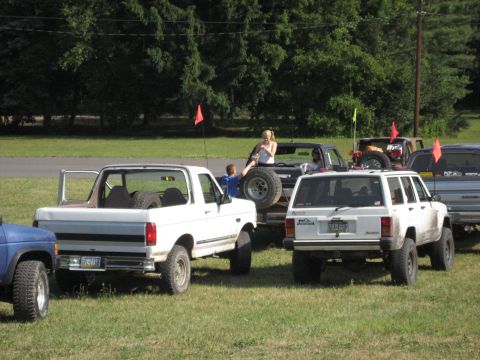 1991 Ford Bronco - Several off-road vehicles are parked on a grassy field under a sunny sky.