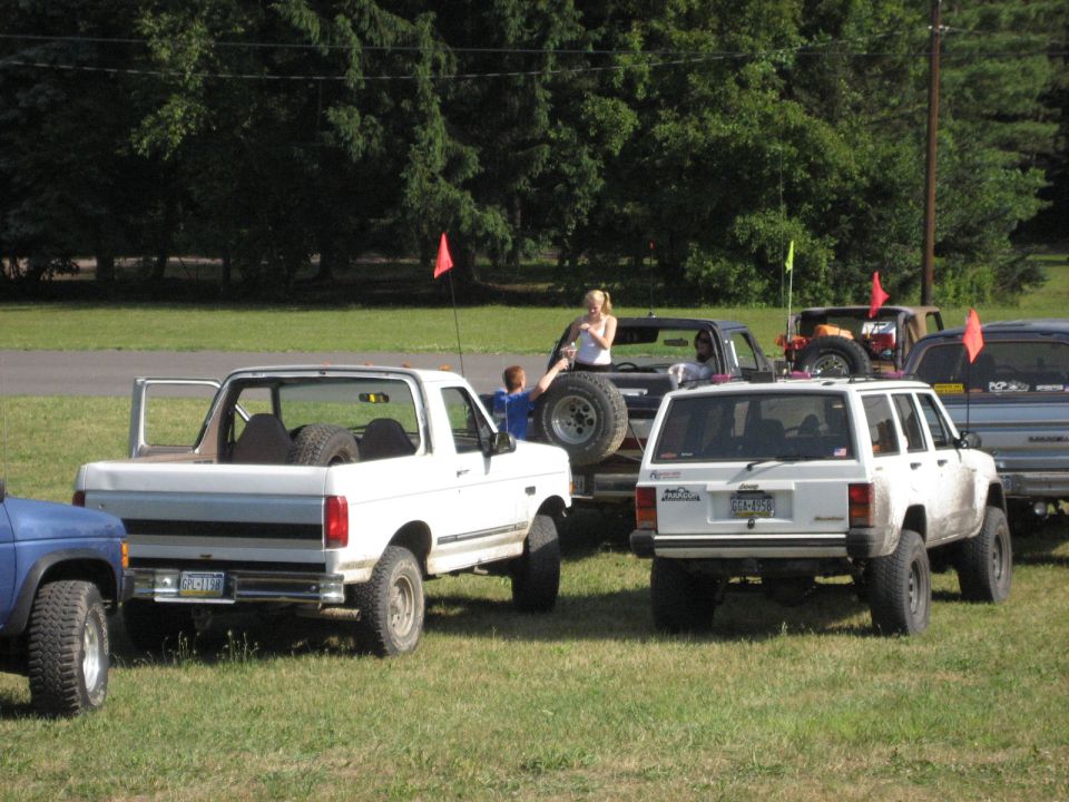 White Ford Bronco with doors open, spare tires in the bed, parked on grass