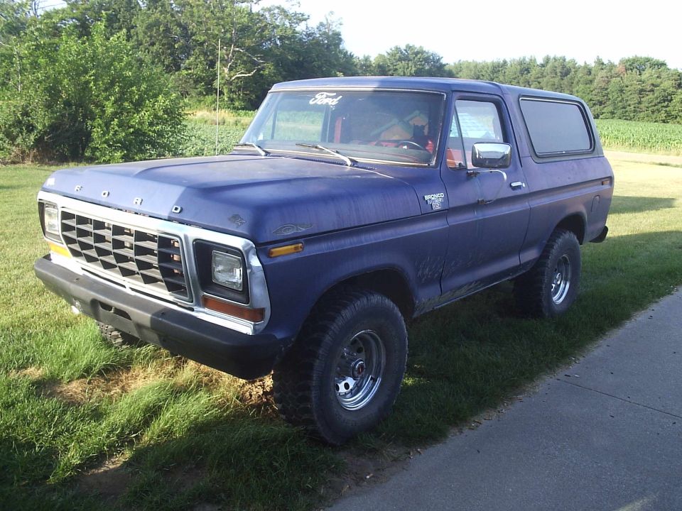 Blue 1978 Ford Bronco parked on grass next to a paved surface