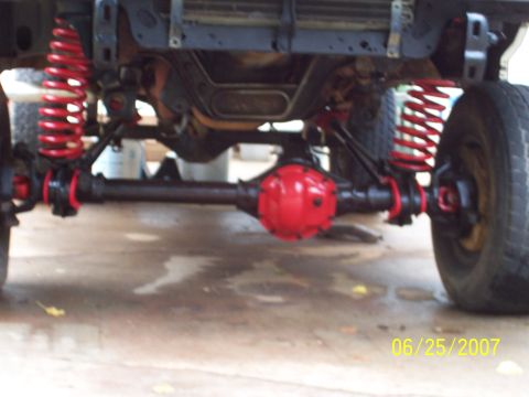 1988 Ford Bronco - The photo shows the modified front suspension and axle of a vehicle, with red coil springs and differential housing.