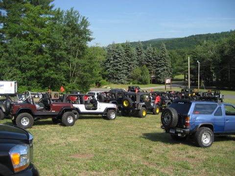 1991 Ford Bronco - A collection of Jeeps and a blue SUV are parked on a grassy field under a clear sky.