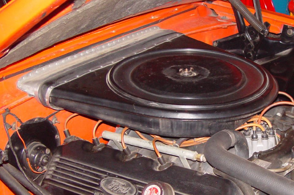 Black oval air cleaner and Ford script valve cover in an orange car's engine bay