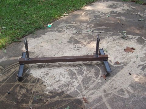 1979 Ford Bronco - A metal axle stand with two upright prongs and four angled legs sits on a concrete surface.