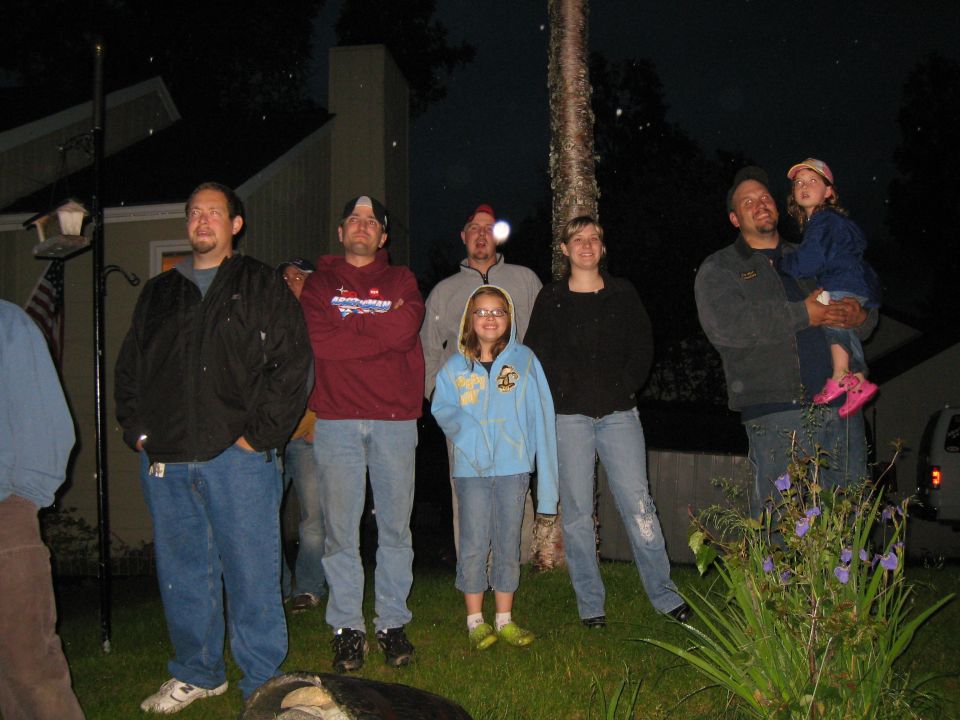Group of people, including children, standing in a yard at night. A portion of a white van is visible on the right