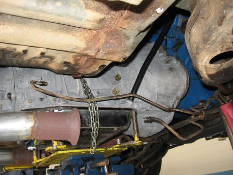 1973 Ford Ranchero - The photo shows the underside of a vehicle, focusing on the transmission and exhaust system, with a chain supporting some of the components.