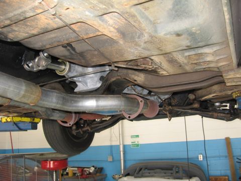 1973 Ford Ranchero - The undercarriage of a vehicle is shown, focusing on the transmission and exhaust components, with a tire visible.