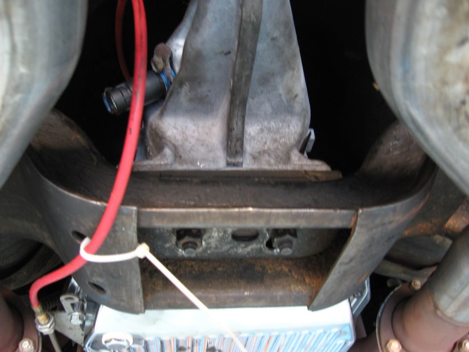 Underbody view of a transmission housing, exhaust pipes, and a red wire