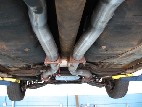 1973 Ford Ranchero - The underside of a vehicle shows a custom dual exhaust system with a driveshaft running above it.