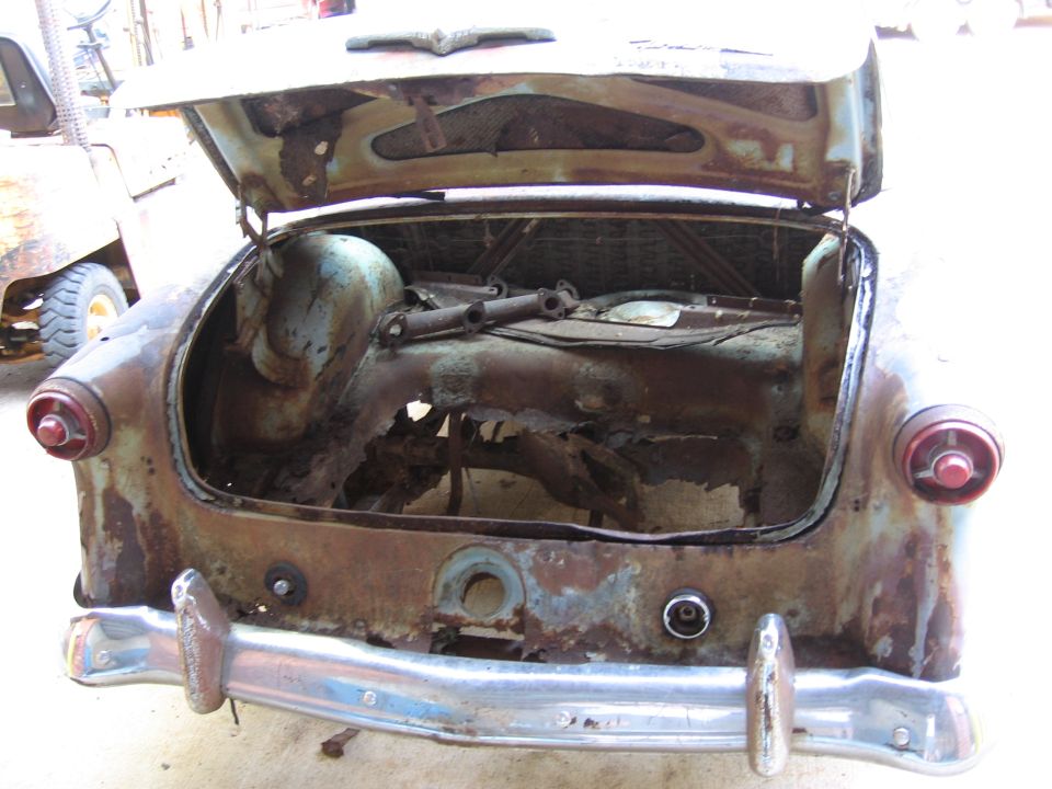 Rusted car trunk with open lid, showing severe damage and missing parts