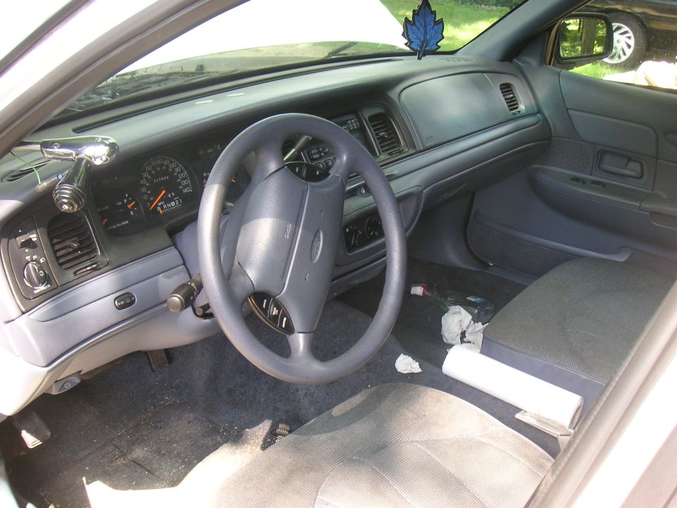 Car interior shot showing dashboard, steering wheel, and seats. A blue air freshener hangs from the rearview mirror