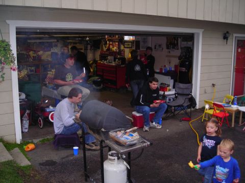 2003 Jeep TJ - A group of people are enjoying a barbecue in a garage with the door open.