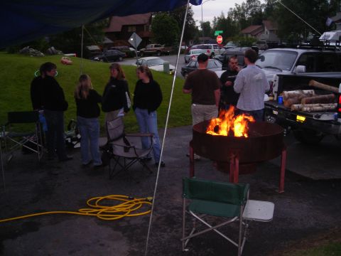 2003 Jeep TJ - A group of people stand around a fire pit during an outdoor gathering, with a pickup truck visible in the background.