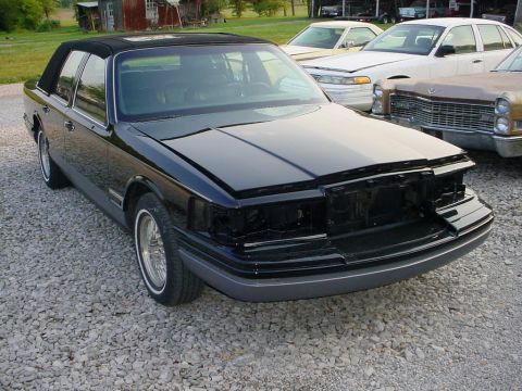 1972 Ford Ranchero - A black sedan with its front end disassembled sits on a gravel lot, with other vehicles visible in the background.