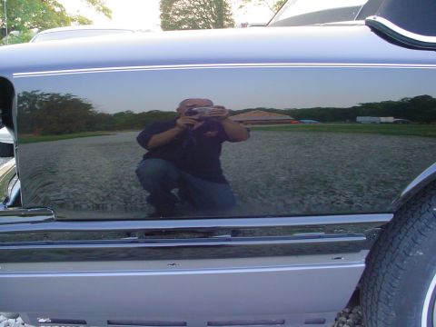 1972 Ford Ranchero - The side panel of a dark vehicle reflects a person holding a camera and the surrounding landscape.