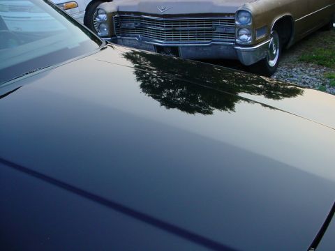 1972 Ford Ranchero - The front of a gold Cadillac is reflected on the polished hood of a dark-colored car.