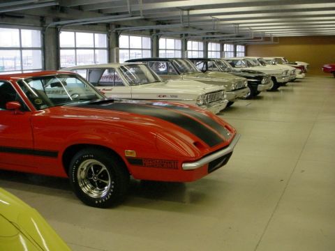1972 Ford Ranchero - A row of classic cars, including a red 1972 Ford Ranchero, are parked indoors.