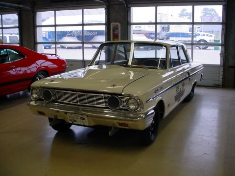 1972 Ford Ranchero - A cream-colored 1964 Ford sedan with racing decals is parked inside a garage next to a red car.