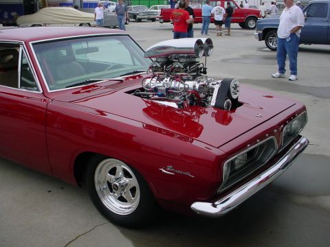 1972 Ford Ranchero - A highly modified red Plymouth Barracuda with a prominent supercharger is parked outdoors, with other vehicles and people in the background.