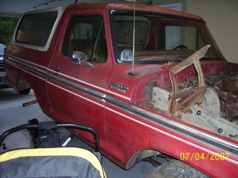 1979 Ford Bronco - This red 1979 Ford Bronco is shown in a garage with its hood removed, revealing its engine bay.