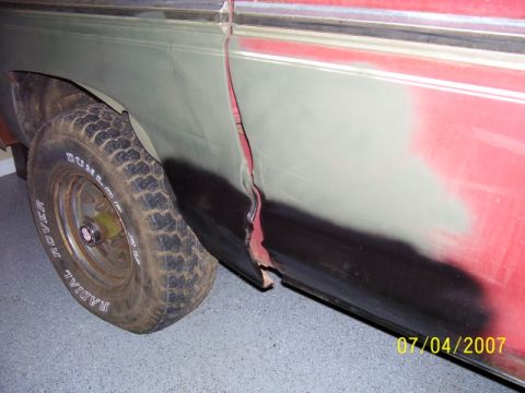 1979 Ford Bronco - Close-up of a vehicle's damaged side panel and fender, showing rust and primer, with a flat tire visible.