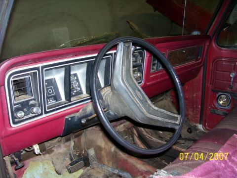 1979 Ford Bronco - The interior of a vintage vehicle shows a red dashboard with gauges and a large steering wheel.