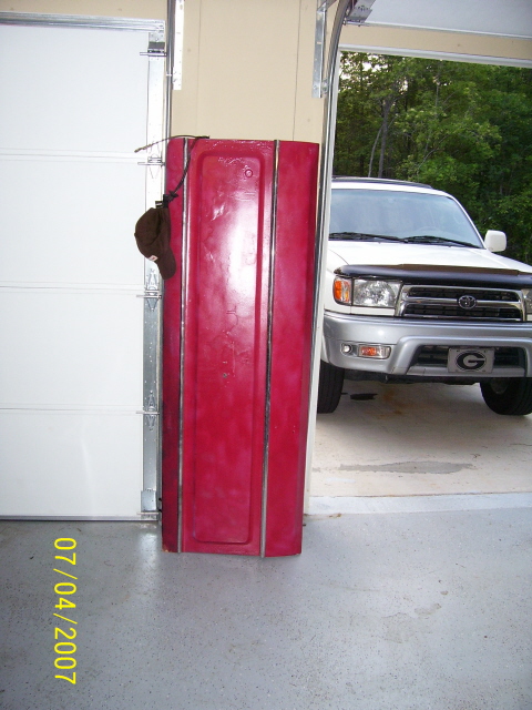 1979 Ford Bronco - A white SUV is visible in the background, parked inside a garage with a red car door in the foreground.
