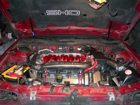 1992 Ford Taurus - The engine bay of a 1992 Ford Taurus SHO features a red intake manifold and prominent SHO badging on the hood liner and intake.