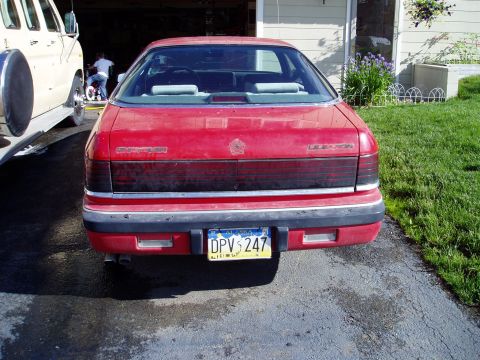 2000 Ford E350 - The rear of a red sedan is visible, parked next to a tan van. The license plate reads DPV 247.