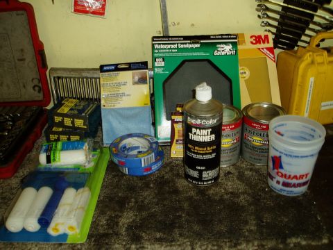 2000 Ford E350 - Various automotive paint supplies including thinner, sandpaper, paint cans, tape, and rollers are laid out on a surface.