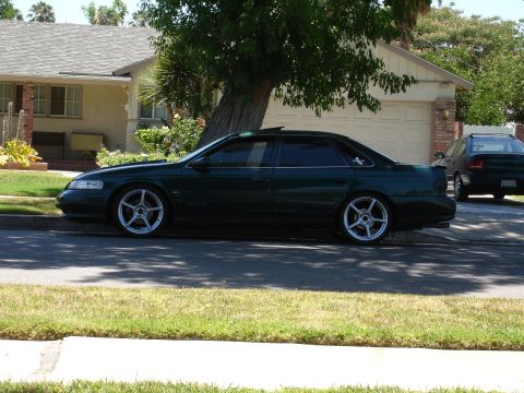 1993 Ford Taurus - Side view of a dark green 1993 Ford Taurus sedan with aftermarket wheels parked on a residential street.
