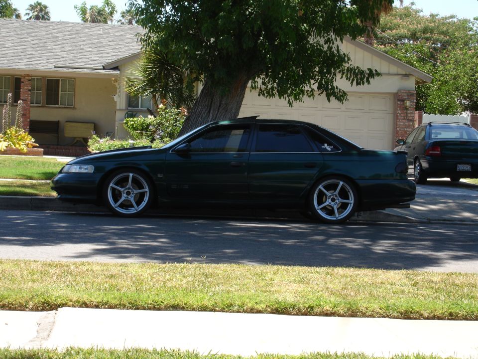 Dark green 1993 Ford Taurus sedan parked on street in front of a house, aftermarket wheels visible