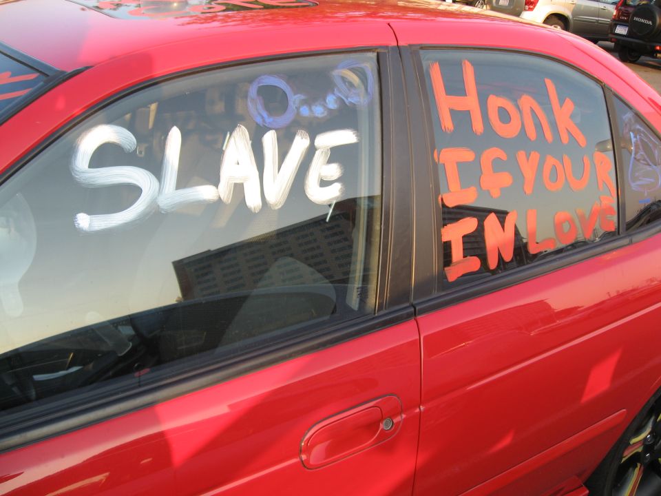 red car windows have 'SLAVE' and 'Honk IF YOUR IN LOVE' written on them