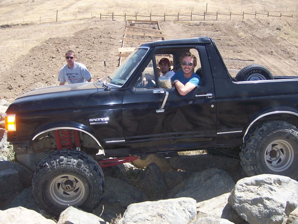Black Ford Bronco with lifted suspension driving over rocks. Three men are inside