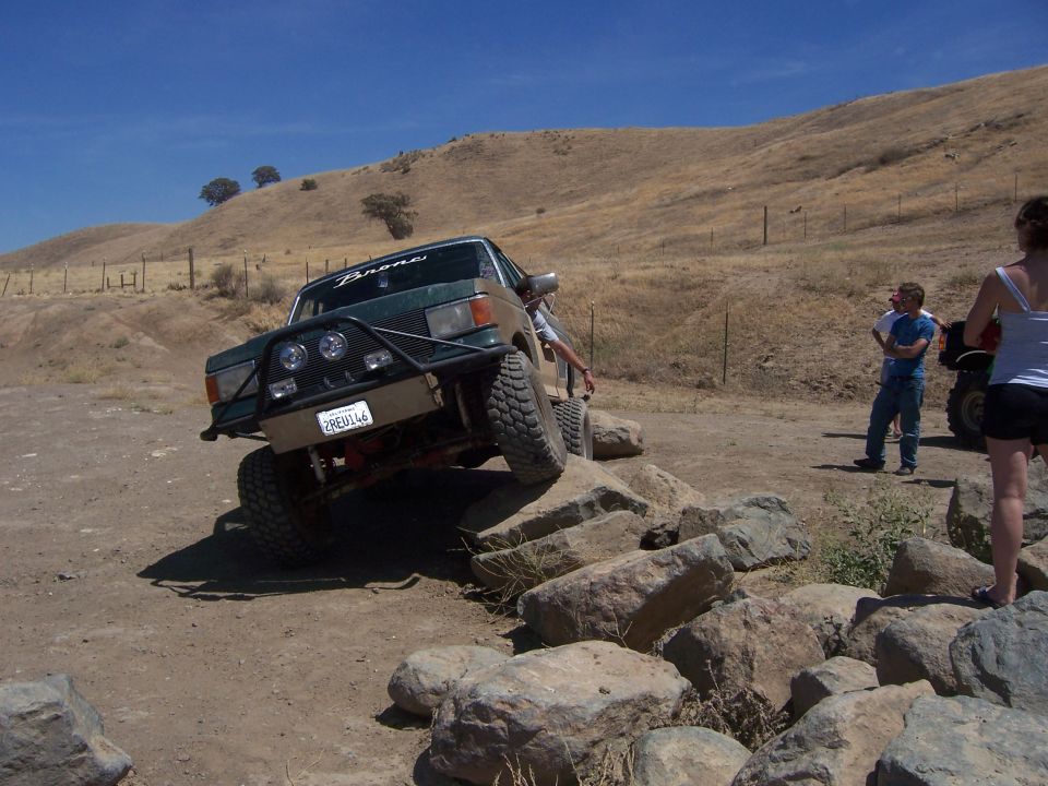 Green Ford Bronco driving over rocks on a dry, grassy hill. License plate reads 2REU146