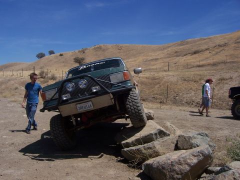 1991 Ford Bronco - A modified green Ford Bronco is shown off-roading on a sunny day.
