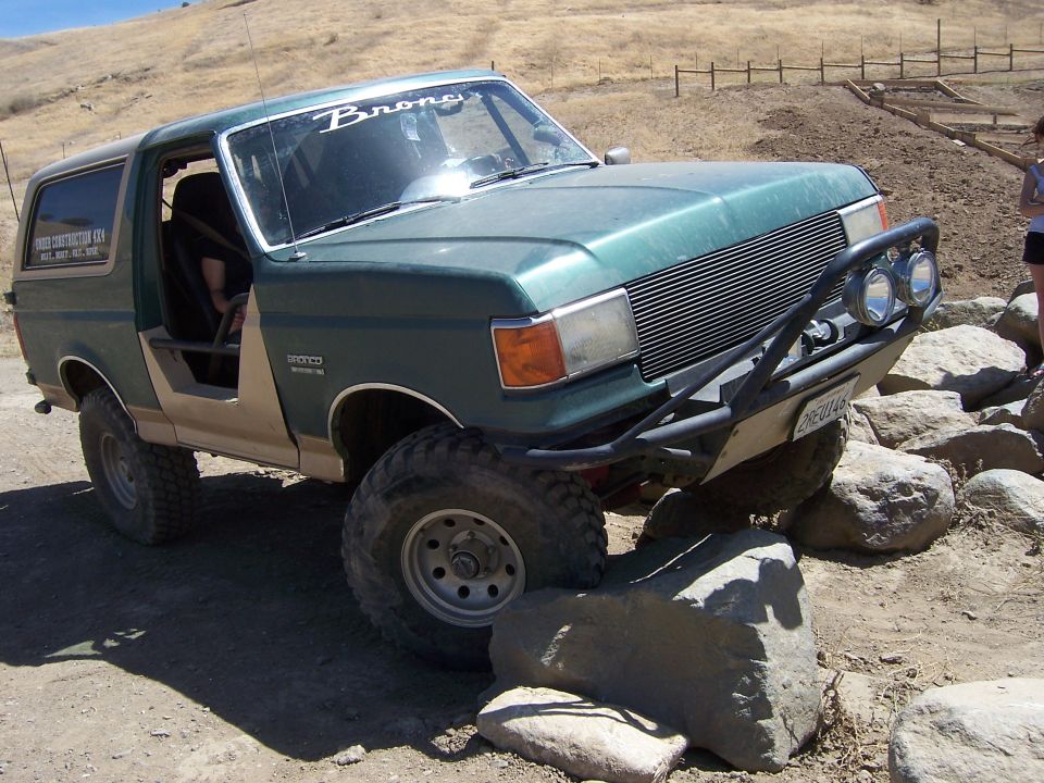 Green Ford Bronco with off-road modifications navigating rocks