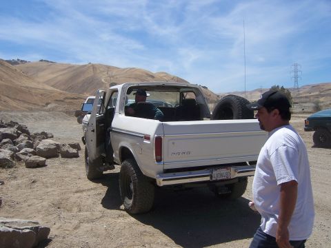 1991 Ford Bronco - White Ford Bronco parked on dirt with a spare tire in the bed. Another vehicle is visible in the background.