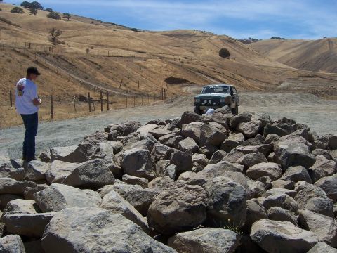 1991 Ford Bronco - A man stands near a pile of rocks, observing a Ford Bronco in a dry, hilly landscape.