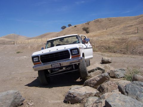 1991 Ford Bronco - A white Ford truck navigates a rocky trail under a clear blue sky.