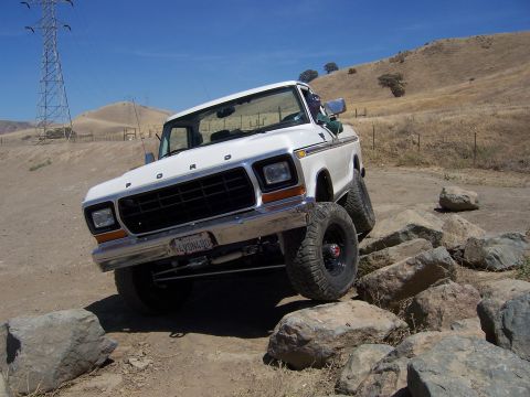 1991 Ford Bronco - A white Ford F-Series truck navigates a rocky terrain under a clear blue sky.
