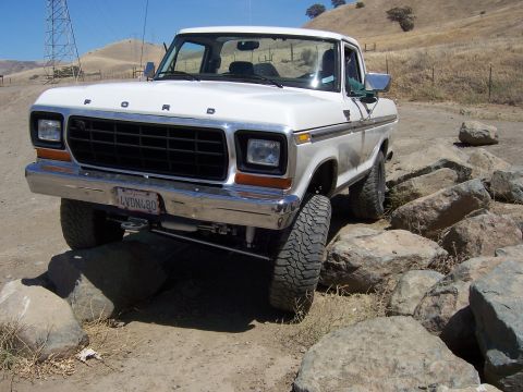 1991 Ford Bronco - White Ford pickup truck with a chrome bumper and grille is shown off-roading over large rocks.