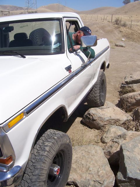 1991 Ford Bronco - This white Ford F-Series truck is shown off-roading over rocks, with its driver visible through the window.