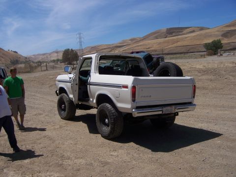 1991 Ford Bronco - A white Ford Bronco with a spare tire in the bed is parked on a dirt road with hills in the background.