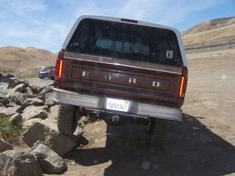 Brown Ford Bronco rear view, white camper shell, off-roading over rocks