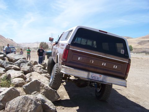 1991 Ford Bronco - A lifted Ford Bronco navigates a rocky trail under a clear blue sky with other vehicles and onlookers present.