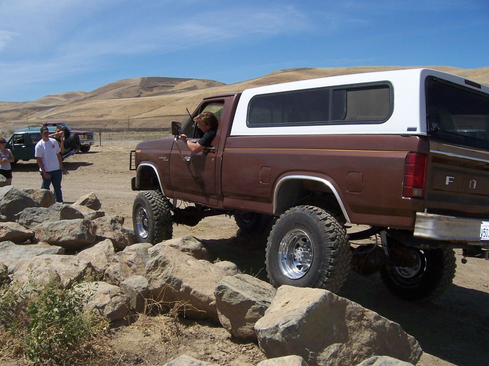 Brown pickup truck with white camper shell on rocky terrain