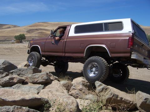 1991 Ford Bronco - This lifted Ford pickup truck navigates a rocky trail under a clear blue sky.