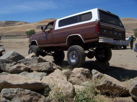 1991 Ford Bronco - Brown Ford Bronco with a white camper shell navigating a rocky terrain.